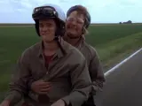 Still image from the Dumb and Dumber movie, showing the duo riding the famous bike with a truck approaching behind them