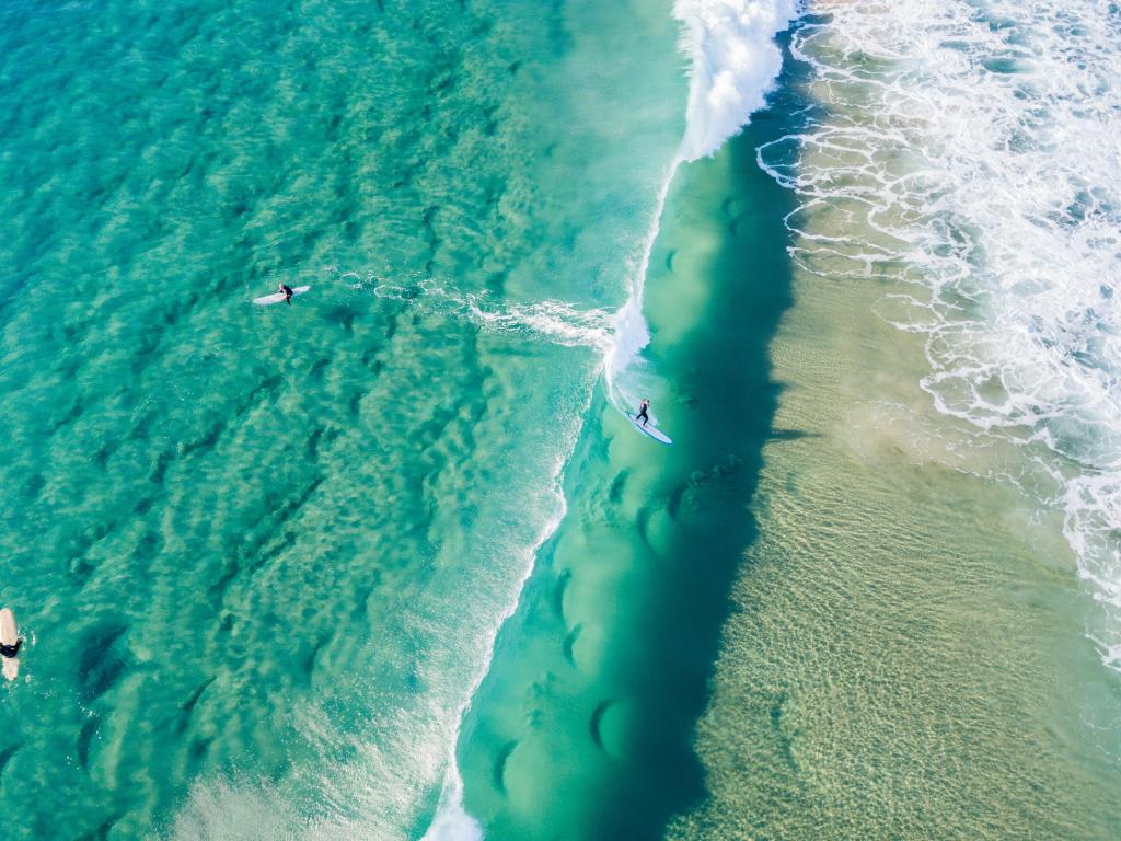 Surfers viewed from above on clear blue sea with white surf