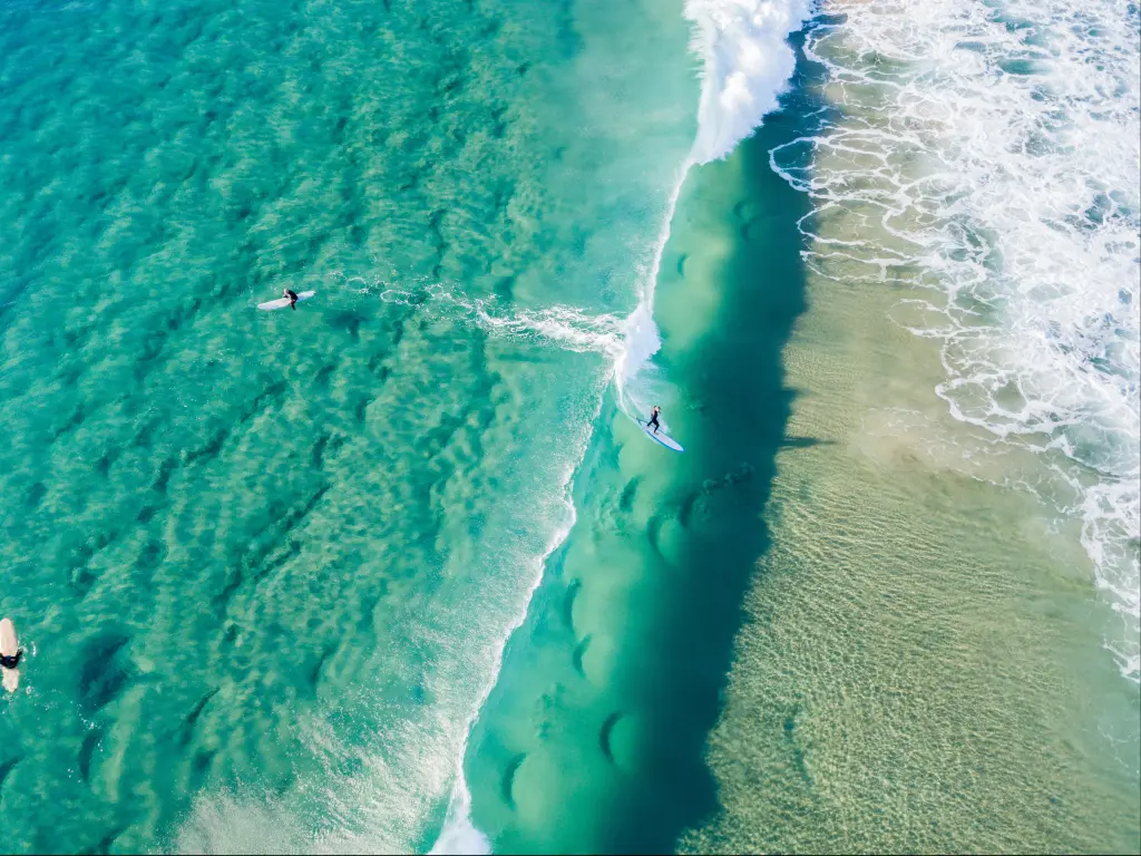 Surfers viewed from above on clear blue sea with white surf