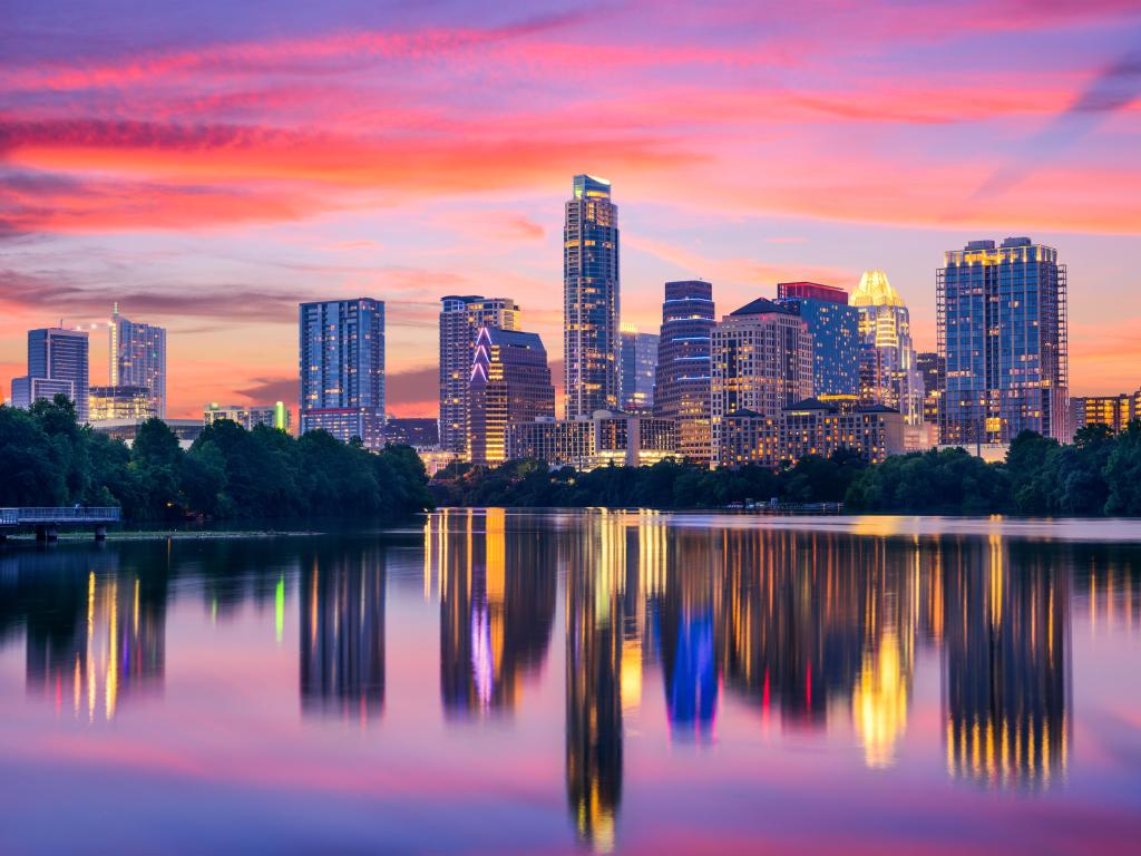 High rise buildings at sunset with a deep pink sky, reflected in still grey water