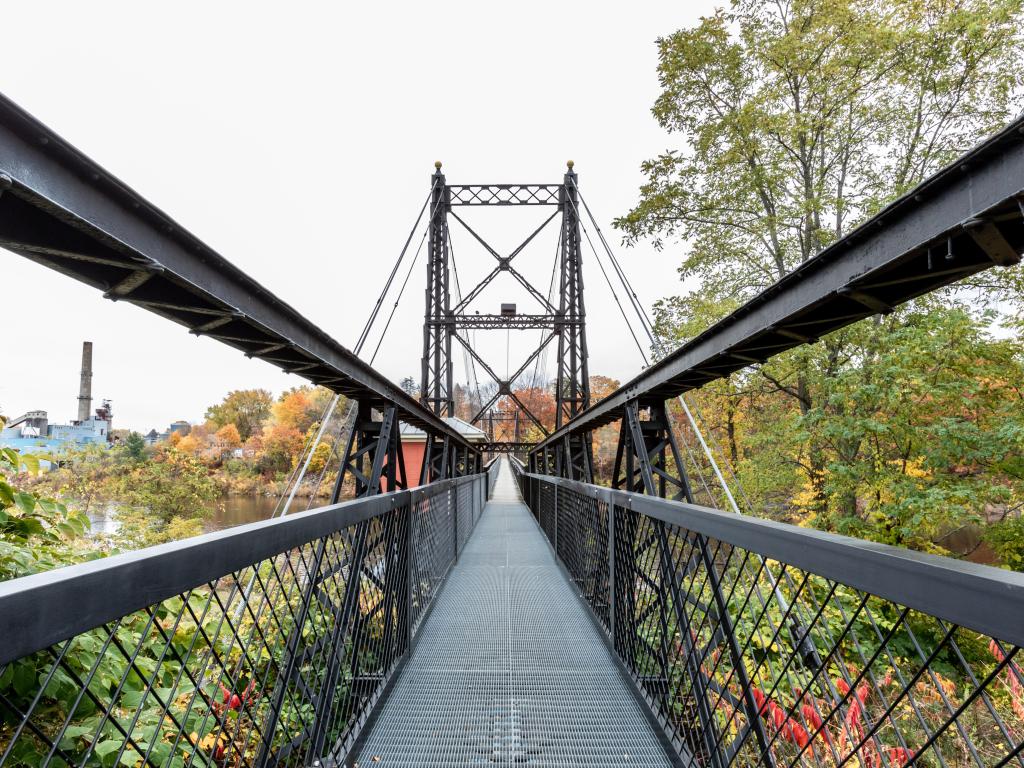 The Ticonic Two Cent Bridge in Waterville, Maine, USA with trees in the distance the city beyond that.