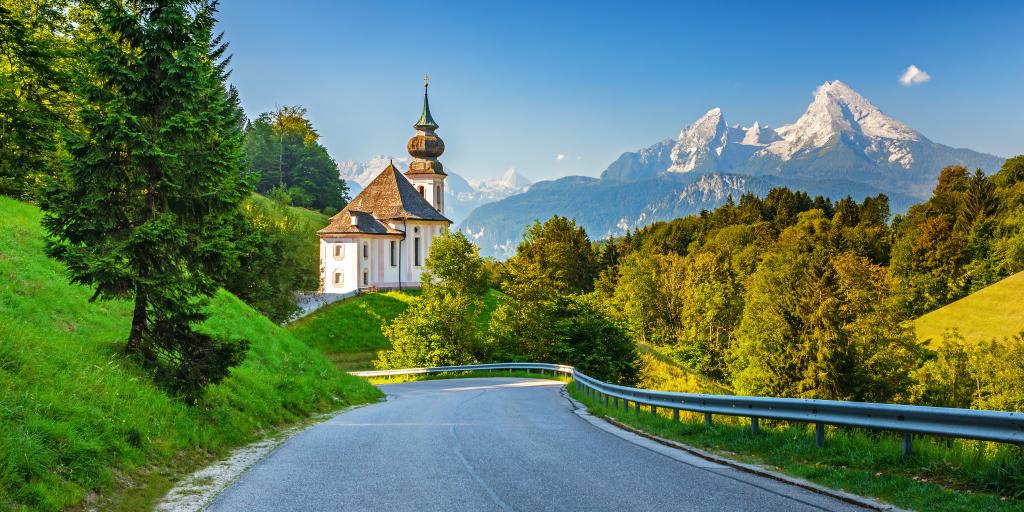 A road with mountains, a church, and trees in the background in the Bavarian Alps