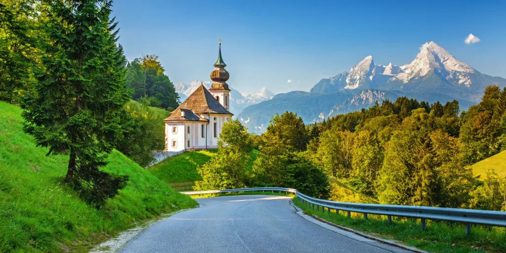 A road with mountains, a church, and trees in the background in the Bavarian Alps