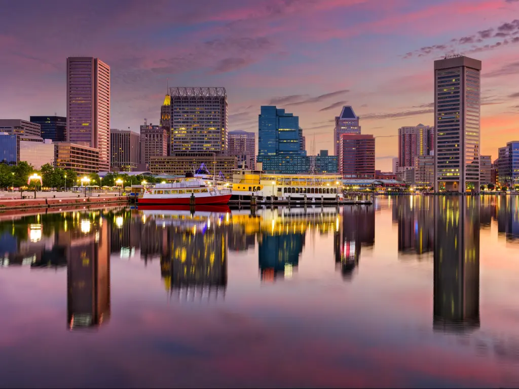 Baltimore, Maryland, USA with the city skyline in the distance at the Inner Harbor, taken at early evening with the city reflecting the water.