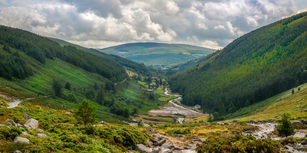 A river cuts through the lush green Glendalough Valley in County Wicklow, Ireland