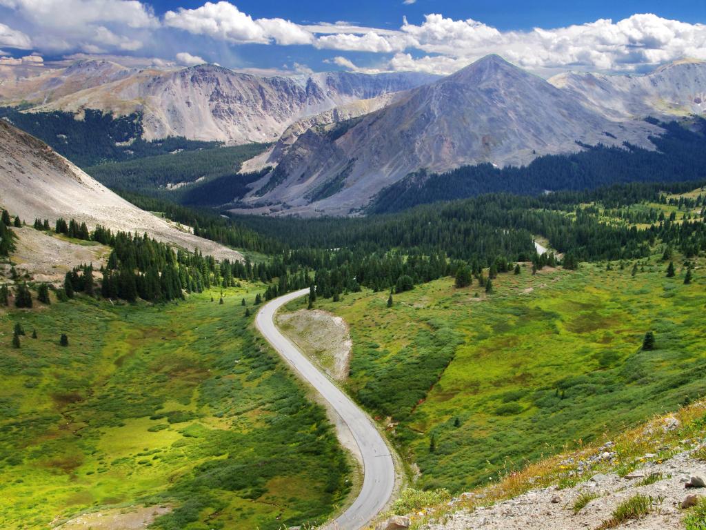 San Isabel National Forest, Colorado, USA taken at Cottonwood Pass with a view of the forest and mountain ranges on a sunny and cloudy day, with a road leading towards them.