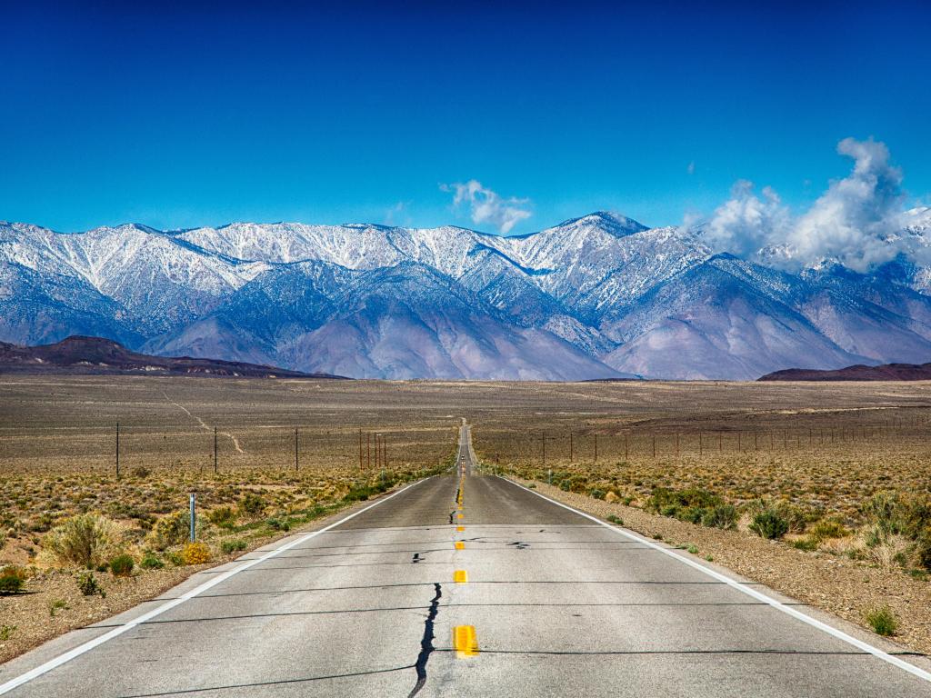 A parched road running through the snow-topped Sierra Nevada mountains in California