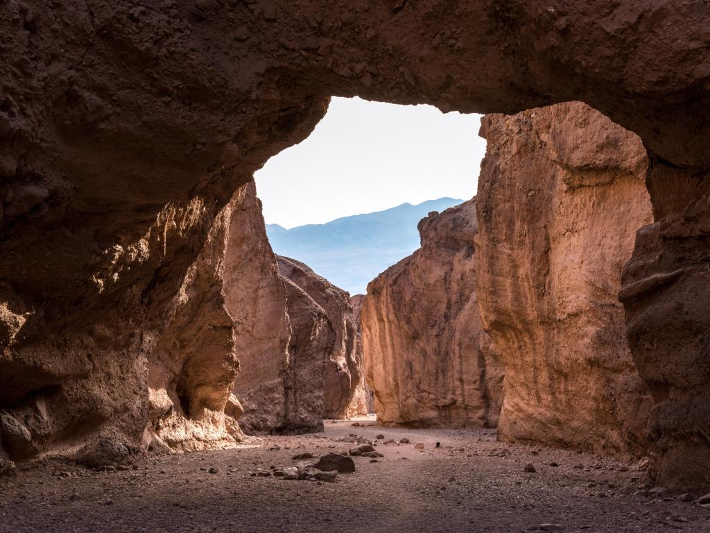 Natural Bridge Canyon, Death Valley National Park, California, USA with an arch in the foreground and cliffs in the distance.