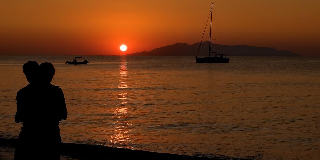 Two people embrace as they watch the sun rise over Santorini, Greece