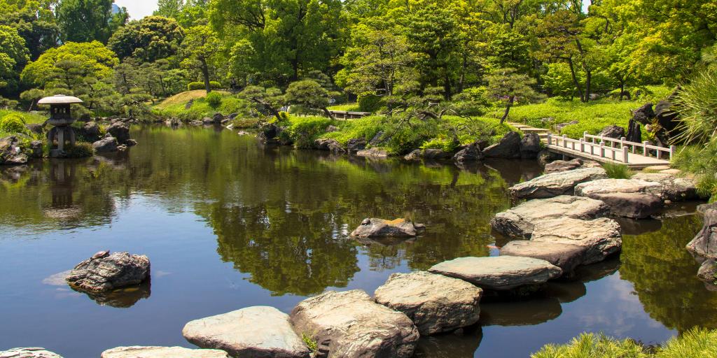 Stepping stones across the water with a bridge and trees in the distance in Kiyosumi Garden