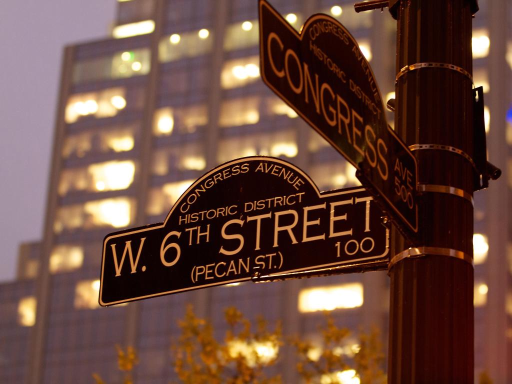 Street signs in Austin, Texas, illuminated in evening light with high rise building behind
