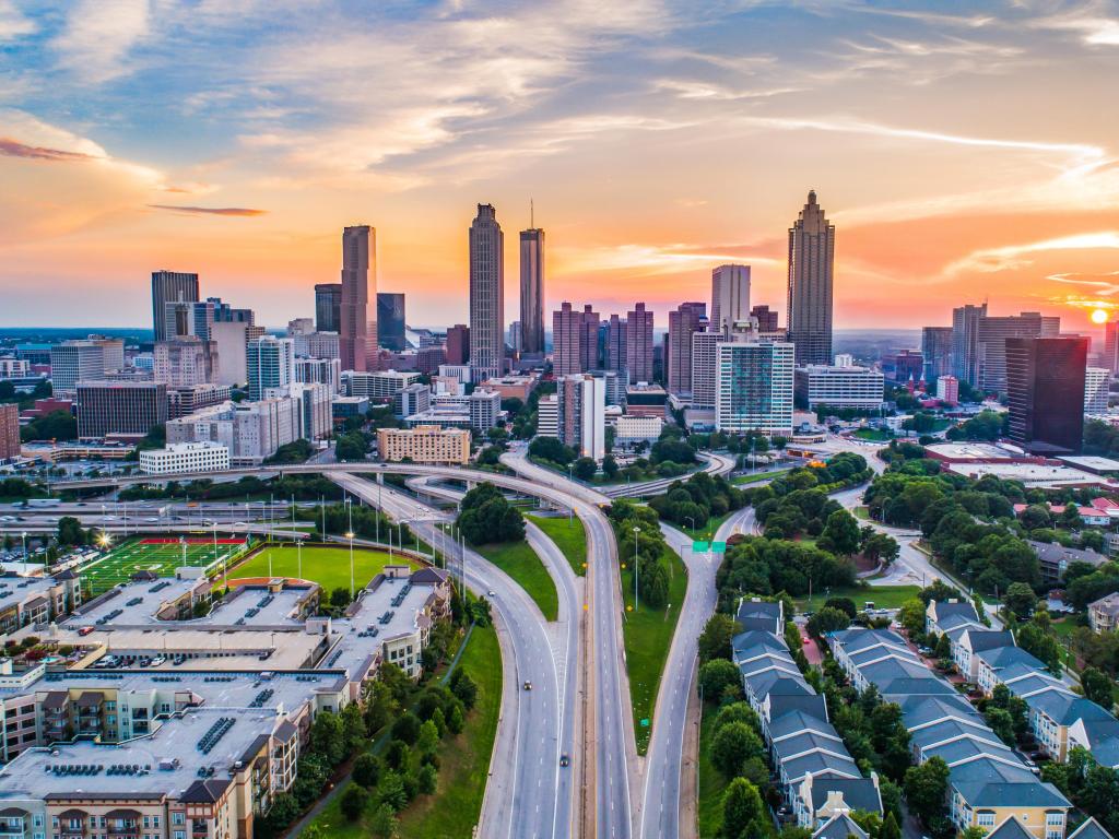 Atlanta, Georgia, USA showing an aerial shot of the downtown skyline at sunset with the skyscrapers in the distance and a network of roads and grass in the foreground. 