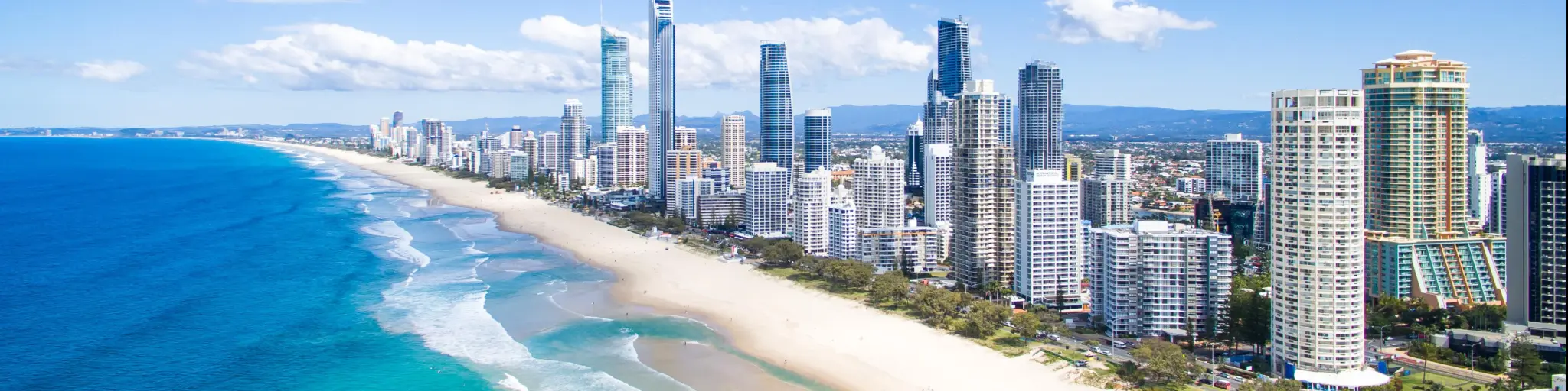 Gold Coast, Australia showing an aerial view of the tall city buildings with the coast and golden sand in the foreground.