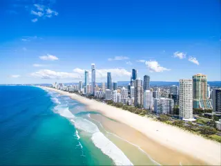 Gold Coast, Australia showing an aerial view of the tall city buildings with the coast and golden sand in the foreground.