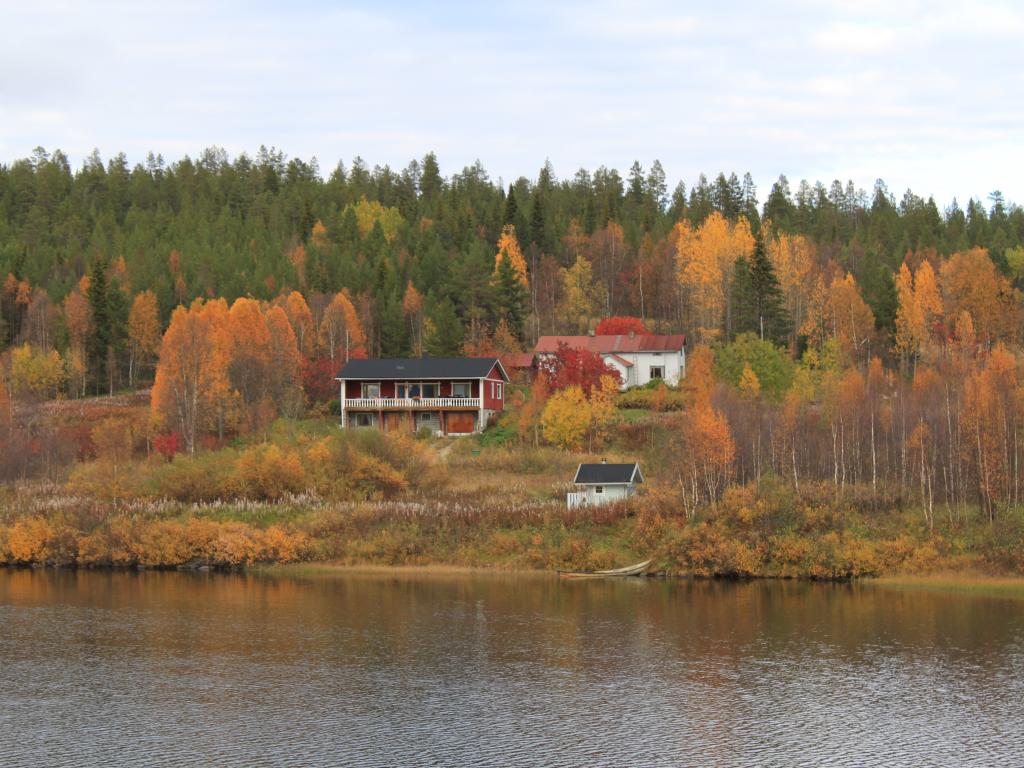 A cabin on a lake on an autumn day is surrounded by colourful trees and evergreens