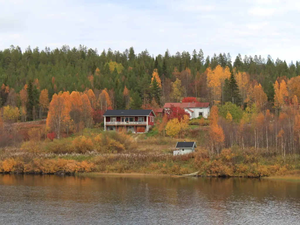 A cabin on a lake on an autumn day is surrounded by colourful trees and evergreens