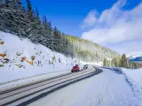 Cars driving through snowy mountain road surrounded by trees