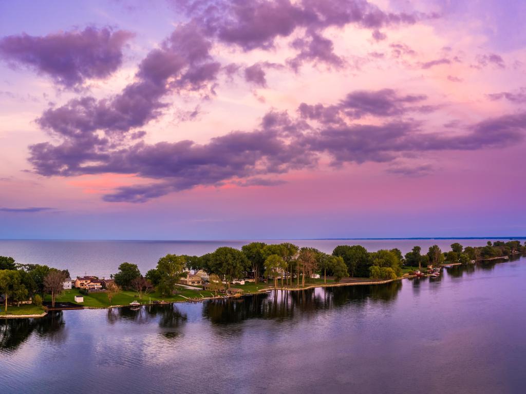 Thin peninsula with houses and trees stretches out across calm water with pink and blue dusk sky