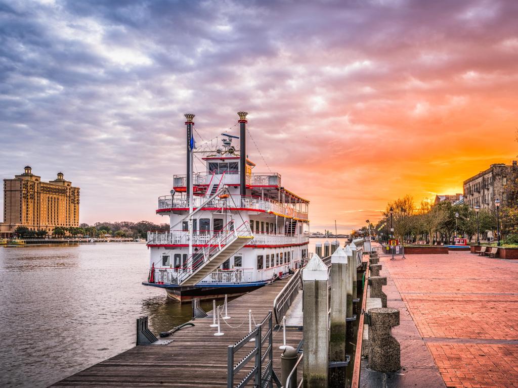 Riverfront promenade at sunrise with pink sky and red and white old fashioned boat moored by the promenade