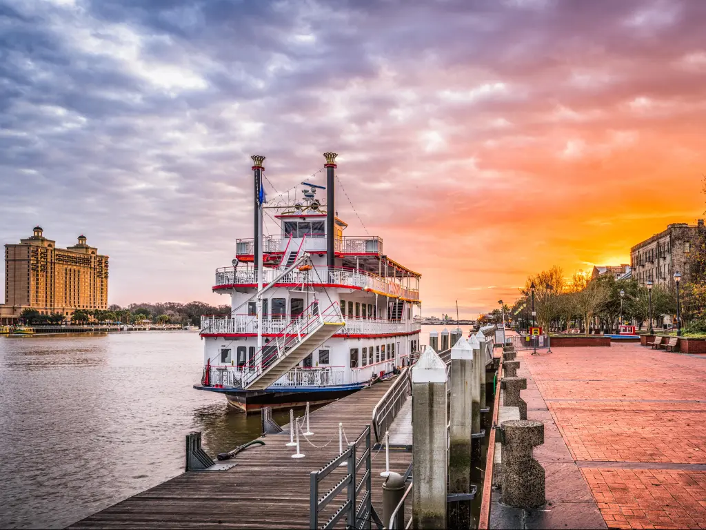 Riverfront promenade at sunrise with pink sky and red and white old fashioned boat moored by the promenade