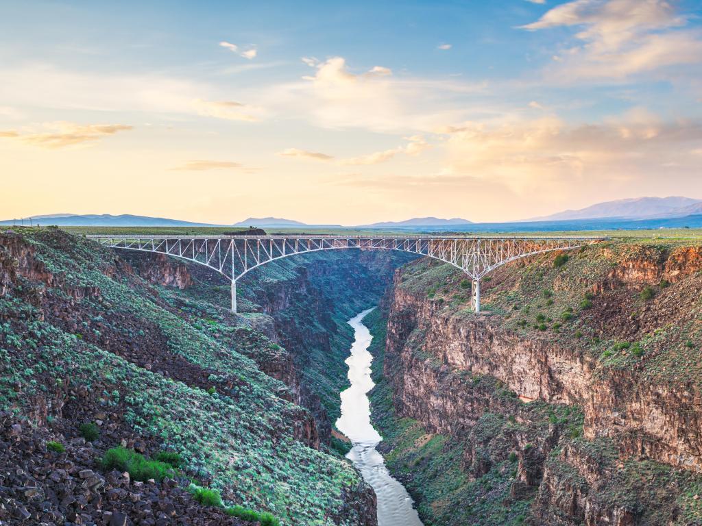 Rio Grande Gorge Bridge, Taos, New Mexico, USA taken at dusk with rocky formations at either side and central to the eye the vast bridge with a river running below. 