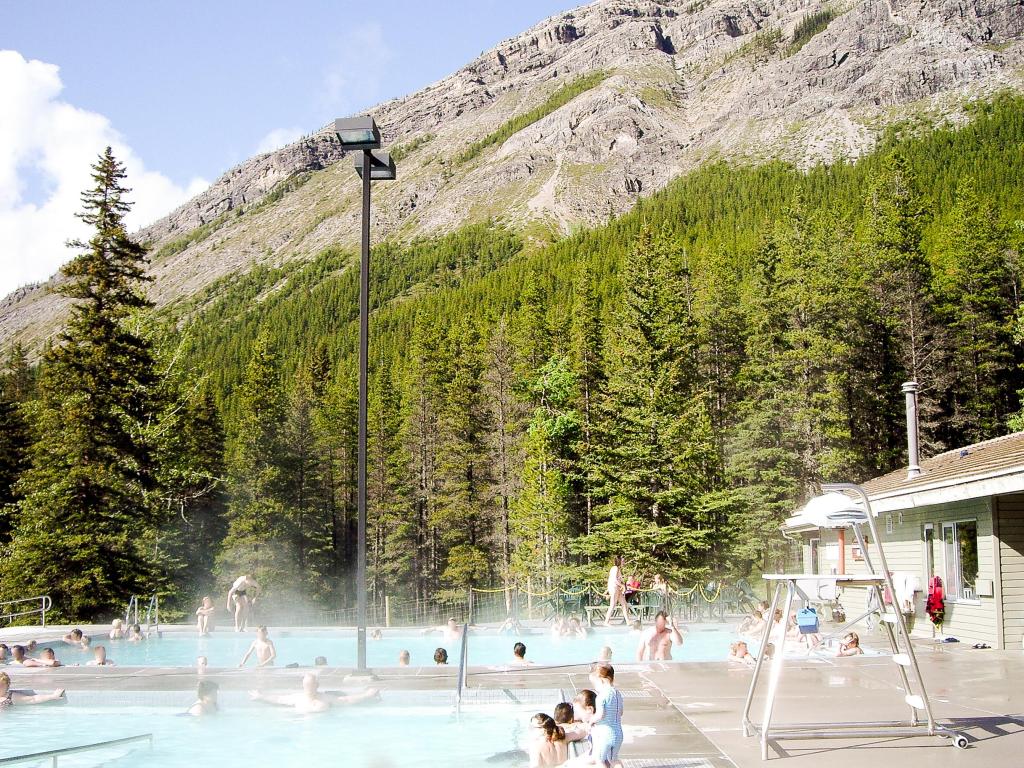 People enjoying a dip in the hot spring pool, there is a hill and forest in the background