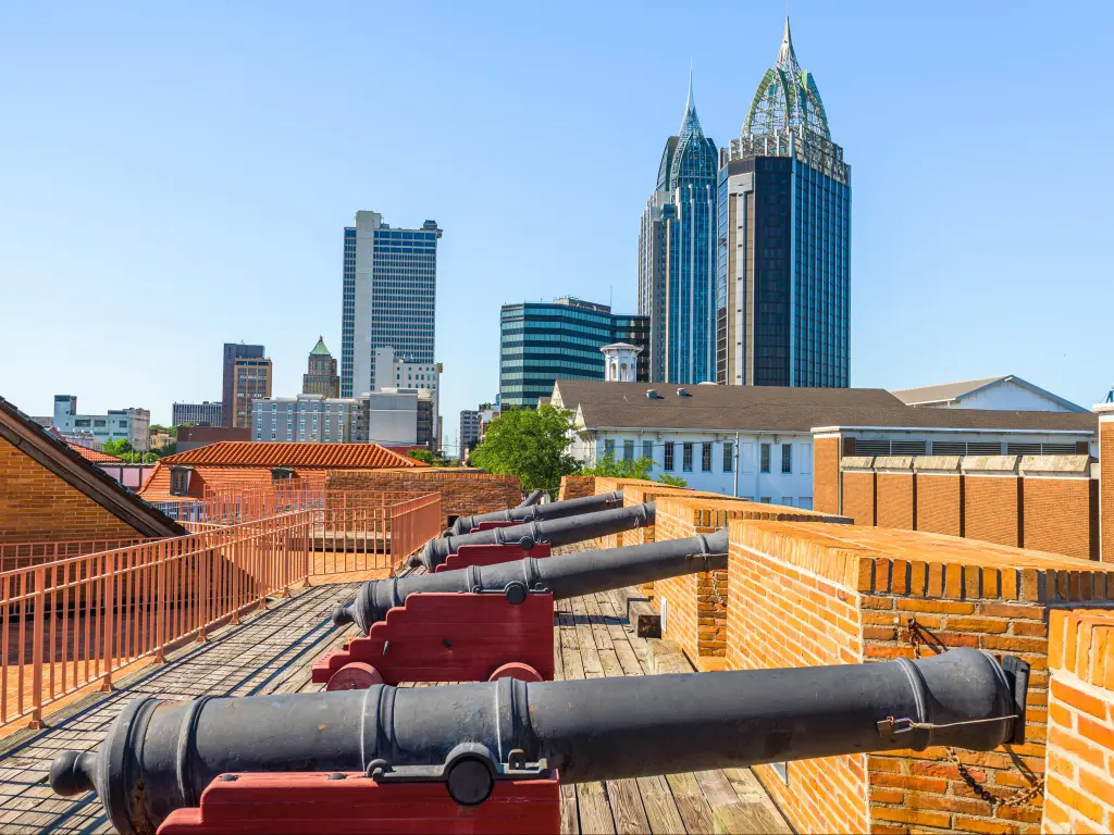 Close up shot of a row of antique canons at a historic fort in Mobile, Alabama, with the city skyline behind