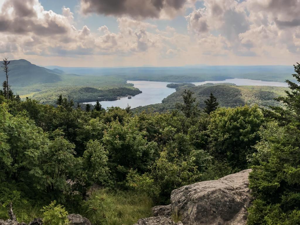 Mont-Orford National Park, Quebec, Canada taken at Mont Chauve on a cloudy but sunny day with trees in the foreground, a lake and mountains in the distance. 