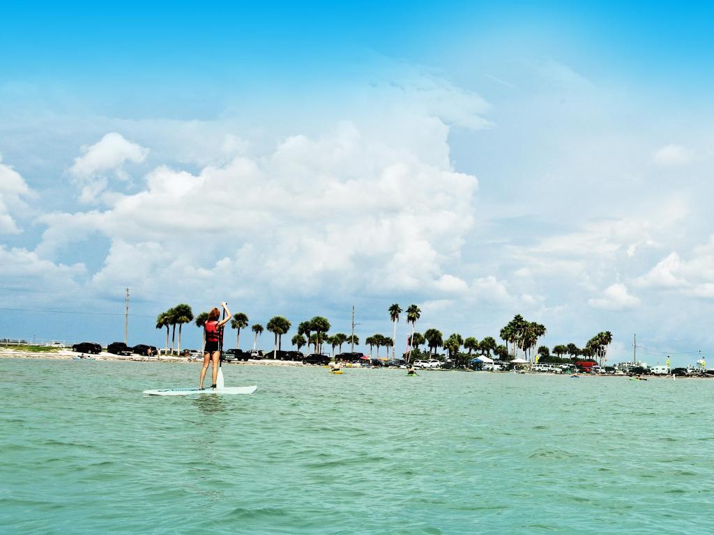 A young woman enjoys the joy of paddle boarding in crystal clear Florida beaches under blue skies in a beautiful Dunedin Causeway
