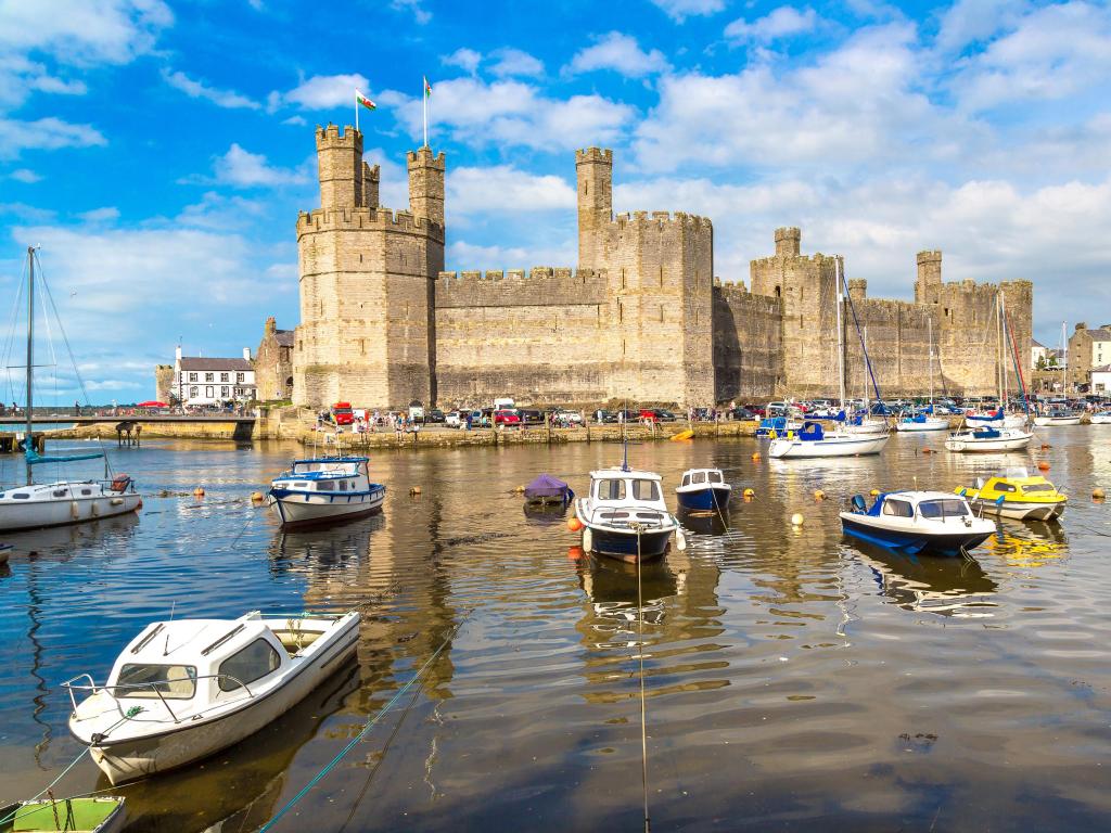 Caernarfon Castle, Wales taken on a beautiful summer day with the harbour and boats in the foreground.