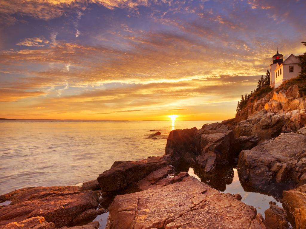 Acadia National Park, Maine, USA with the Bass Harbor Head Lighthouse on the edge of the photo, rocky formations in the foreground and taken during sunset on a calm day with the sea leading to the distance.  