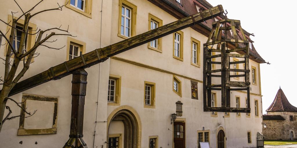 A Medieval dunking cage hanging from the outside of a cream and yellow building