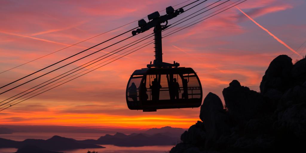   A silhouette of the Dubrovnik Cable Car at sunset against an orange and pink sky