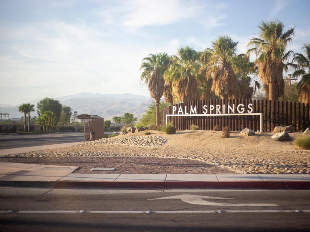 City of Palm Springs, California, USA on a clear sunny day with the sign and palm trees and a road leading towards the mountains. 