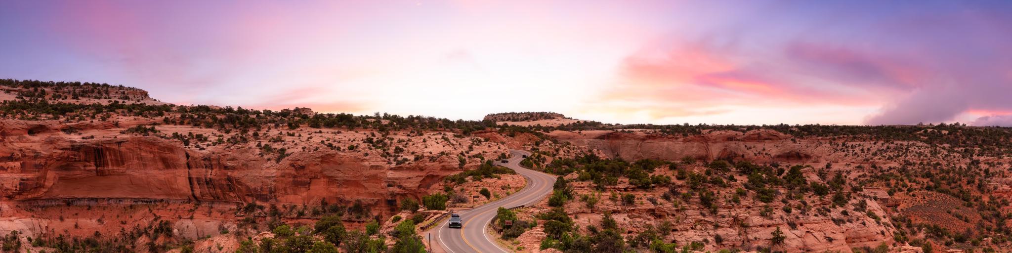 Scenic road running through Canyonlands National Park beneath a purple-hued sunset sky, with red rocks on the horizon