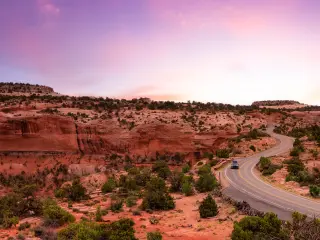 Scenic road running through Canyonlands National Park beneath a purple-hued sunset sky, with red rocks on the horizon