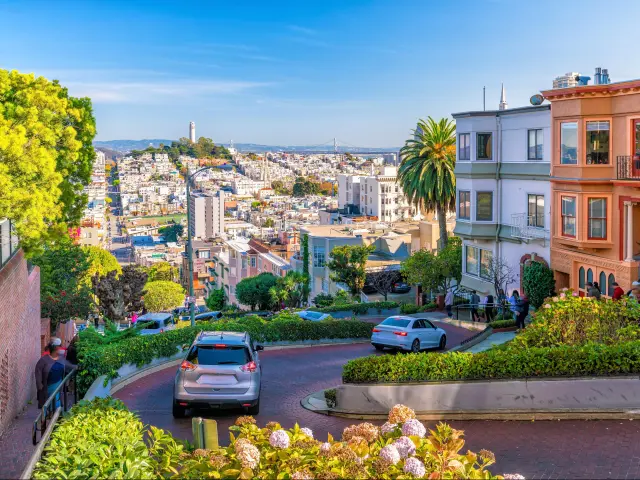 Steep winding Lombard Street in San Francisco leading to the city centre, colourful buildings on the right and the bridge in the far distance.