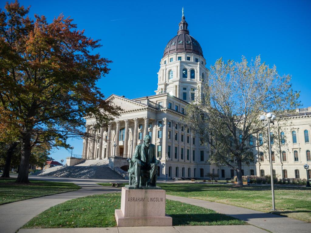 Kansas State Capitol building in Topeka with a statue of Lincoln in front and a blue sky above