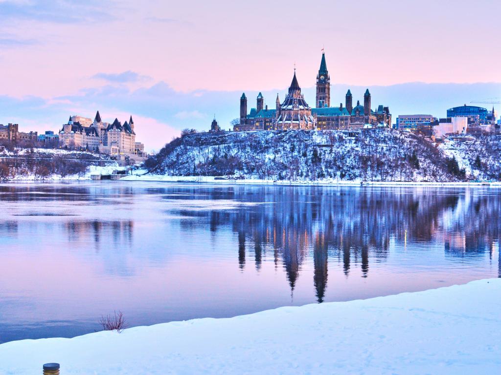 Church on cliff reflected in still river water with snow and ice and pink and blue light