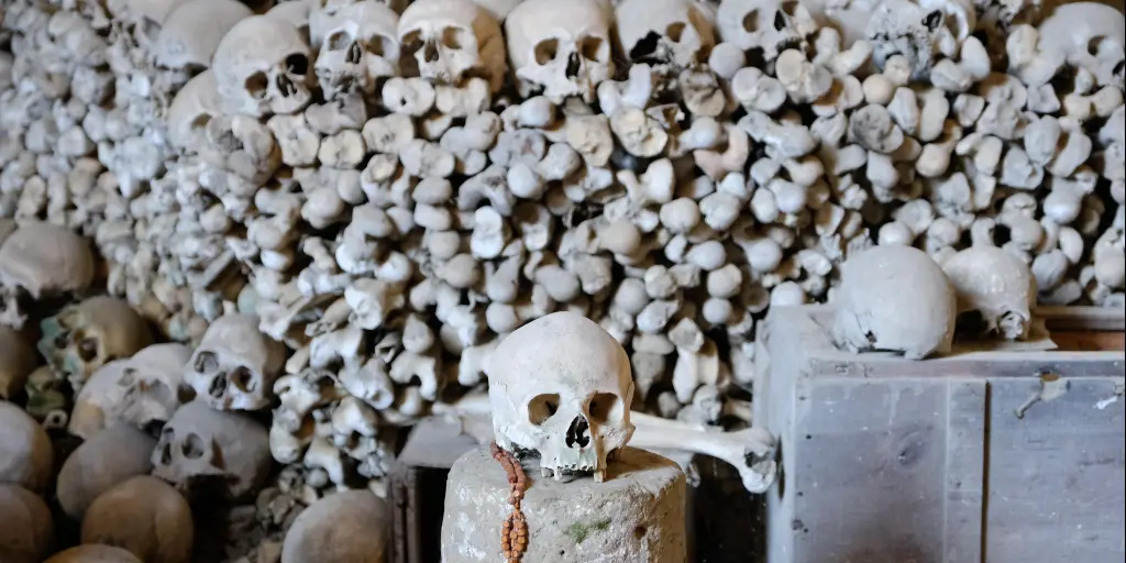 A skull with some rosary beads and piles of skulls and bones in the background