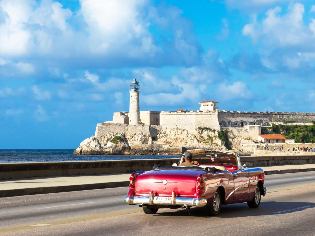 American red convertible Buick 50 Super 1954 vintage car on the Malecon on a sunny day. You can see Castillo del Morro in the background. Photo is taken in Havana, Cuba.