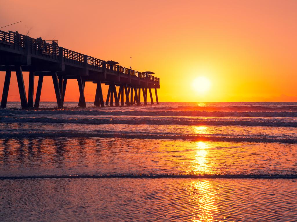 Sun rising over horizon and pier, beach illuminated with sunlight, Beautiful sunrise in Florida. Jacksonville Florida, USA.