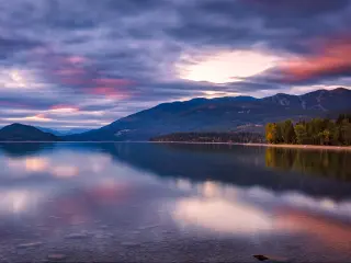 Whitefish Lake, Montana with a stunning sunset sky of pinks and purples, mountains in the distance reflecting in the water and green land either side.