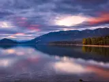 Whitefish Lake, Montana with a stunning sunset sky of pinks and purples, mountains in the distance reflecting in the water and green land either side.