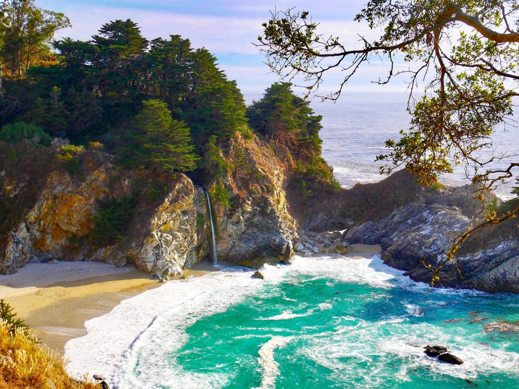 McWay Falls in Julia Pfeiffer State Park, Big Sur, California, USA with a view of the bay surrounded by cliffs and trees.