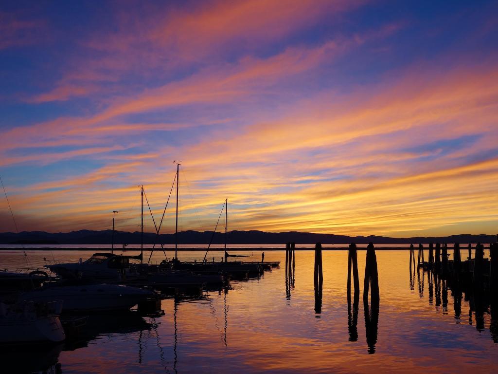 Lake Champlain, Burlington, Vermont, USA taken at sunset with the stunning sky reflected in the lake with wispy orange clouds reflected on the water, boats and a pier in silhouette.