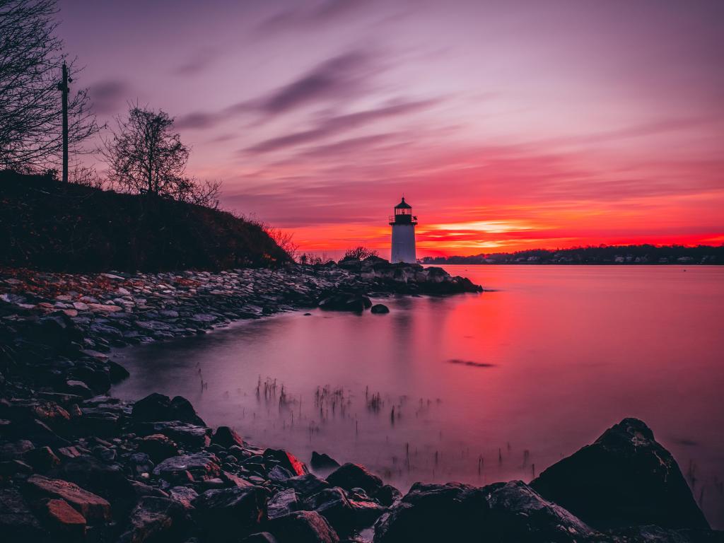 White lighthouse at the end of a bay with pink sunrise