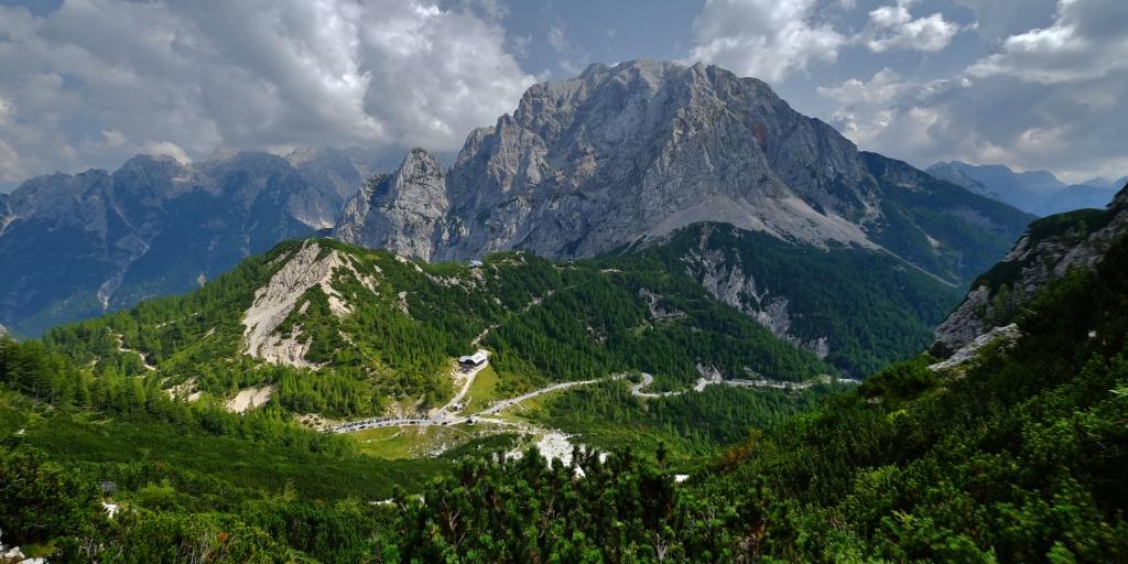 Vrsic Pass, Slovenia road across green hill with a rocky mountain in the background 