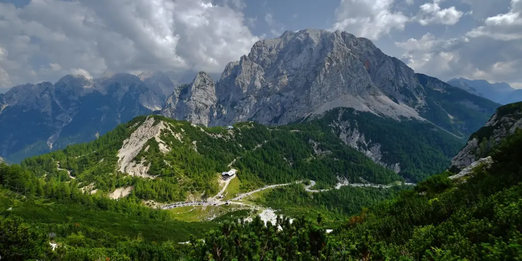 Vrsic Pass, Slovenia road across green hill with a rocky mountain in the background 