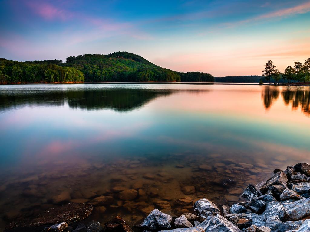 Lake Allatoona, Atlanta, USA at Red Top Mountain State Park north of Atlanta at sunrise with rocks in the foreground and tree-covered hills in the distance reflected in the lake.